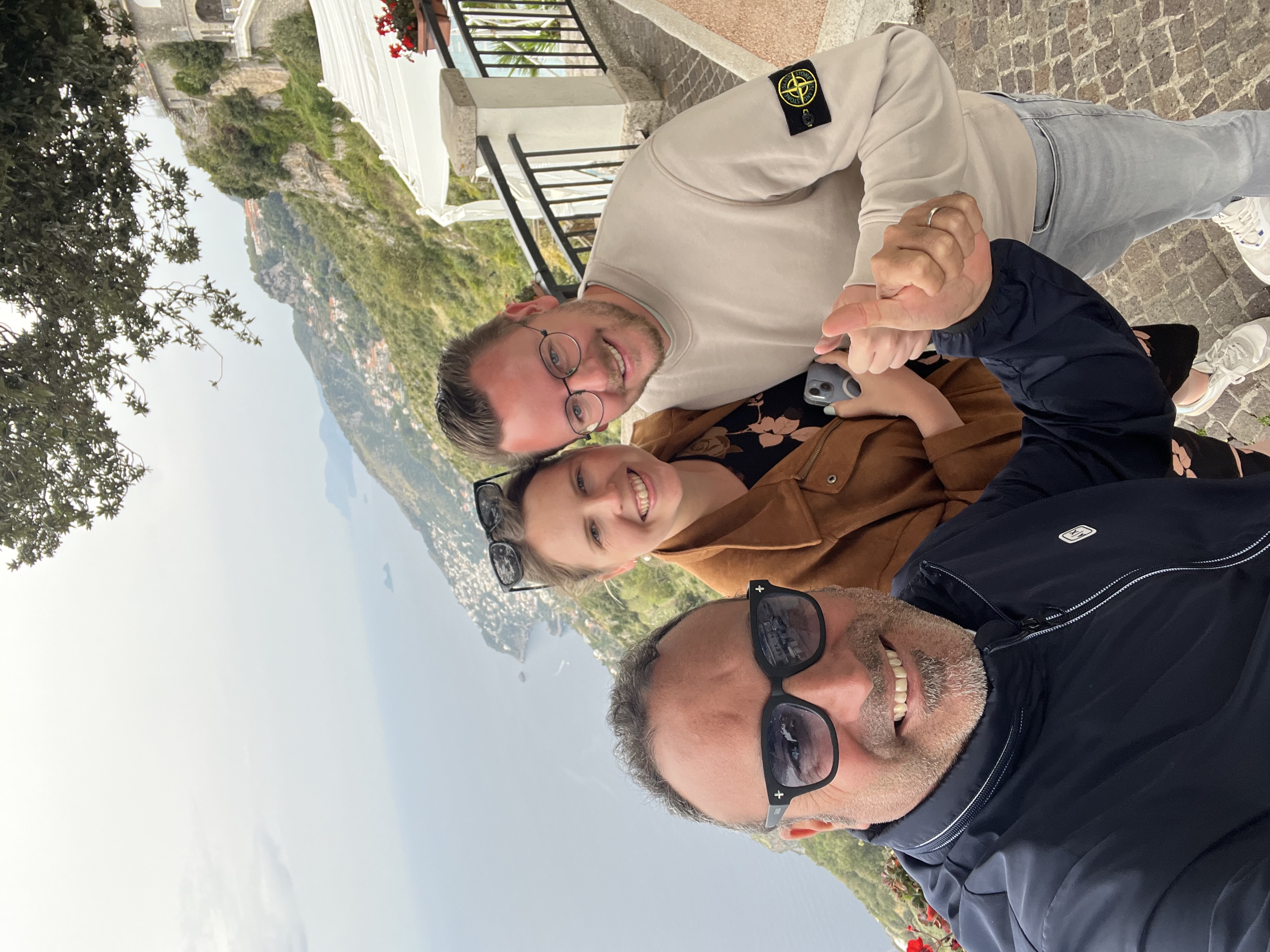 Group posing on scenic overlook with ocean and hills.