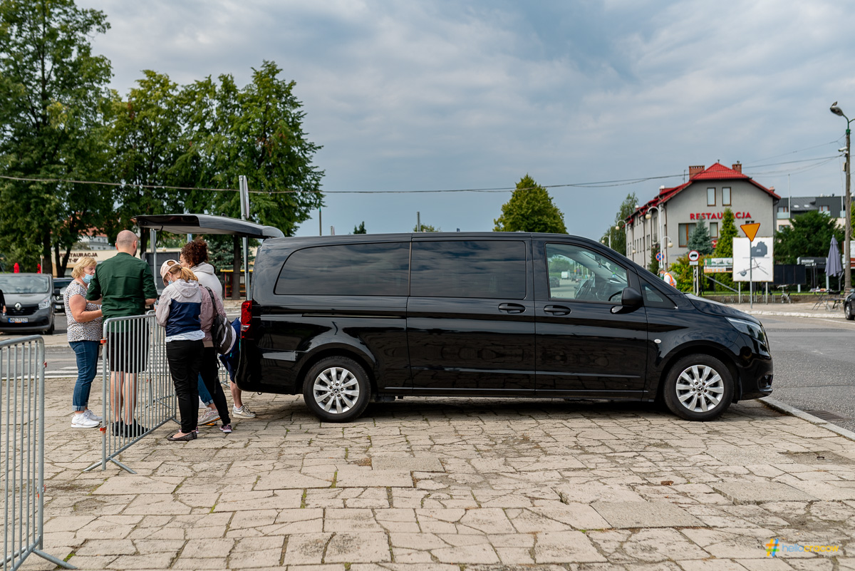 Black van parked on a paved area, with people standing nearby.