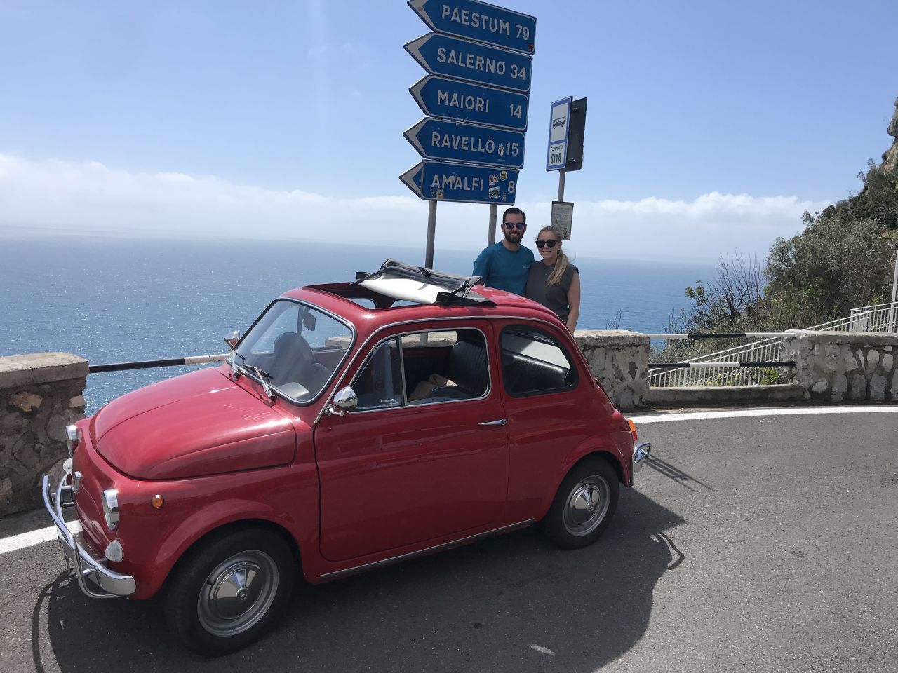 Red vintage car parked near road signs, overlooking the sea.