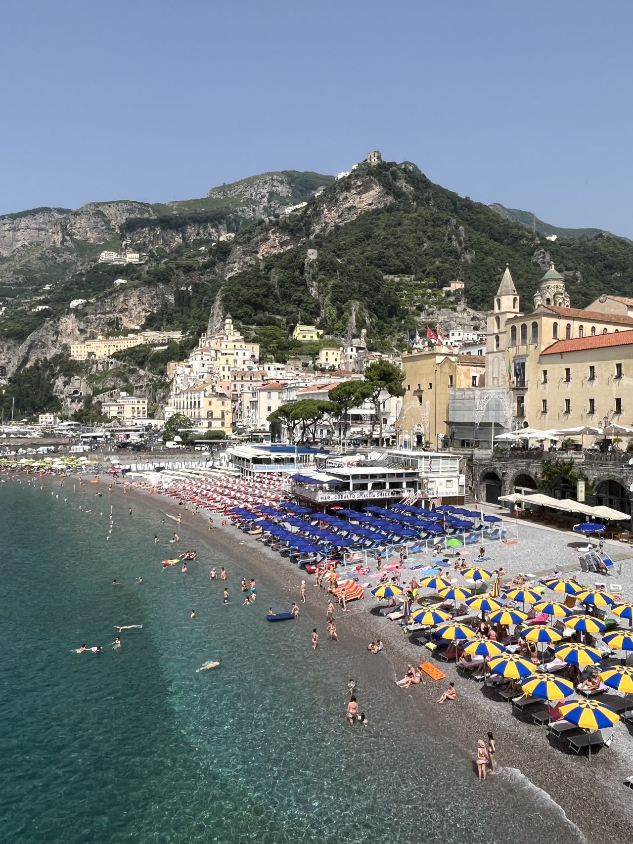 Crowded beach with colorful umbrellas along a scenic coastline.