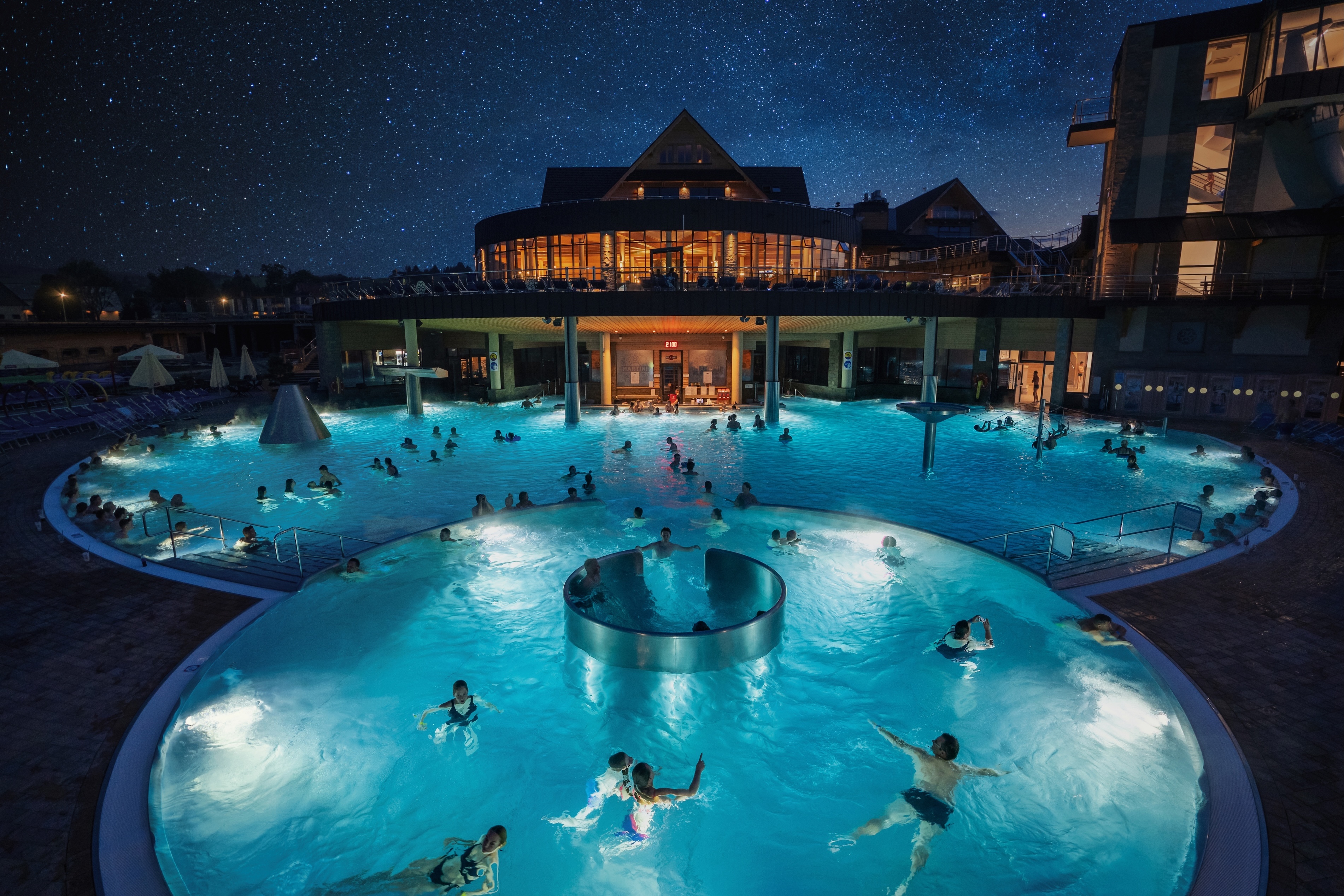 Nighttime view of outdoor pool with people swimming, under a starry sky.