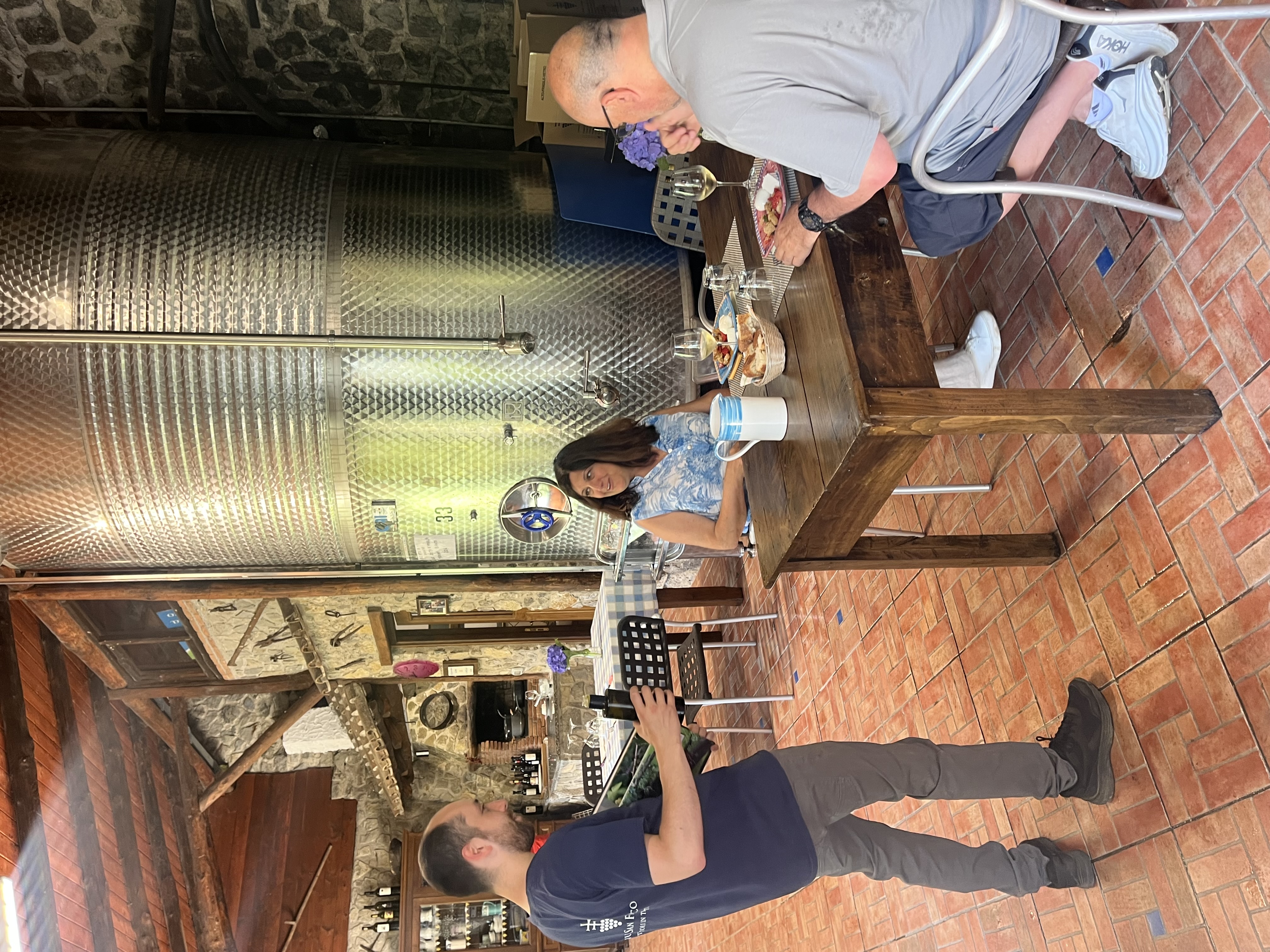 Two people dining at a table near large wine barrels.