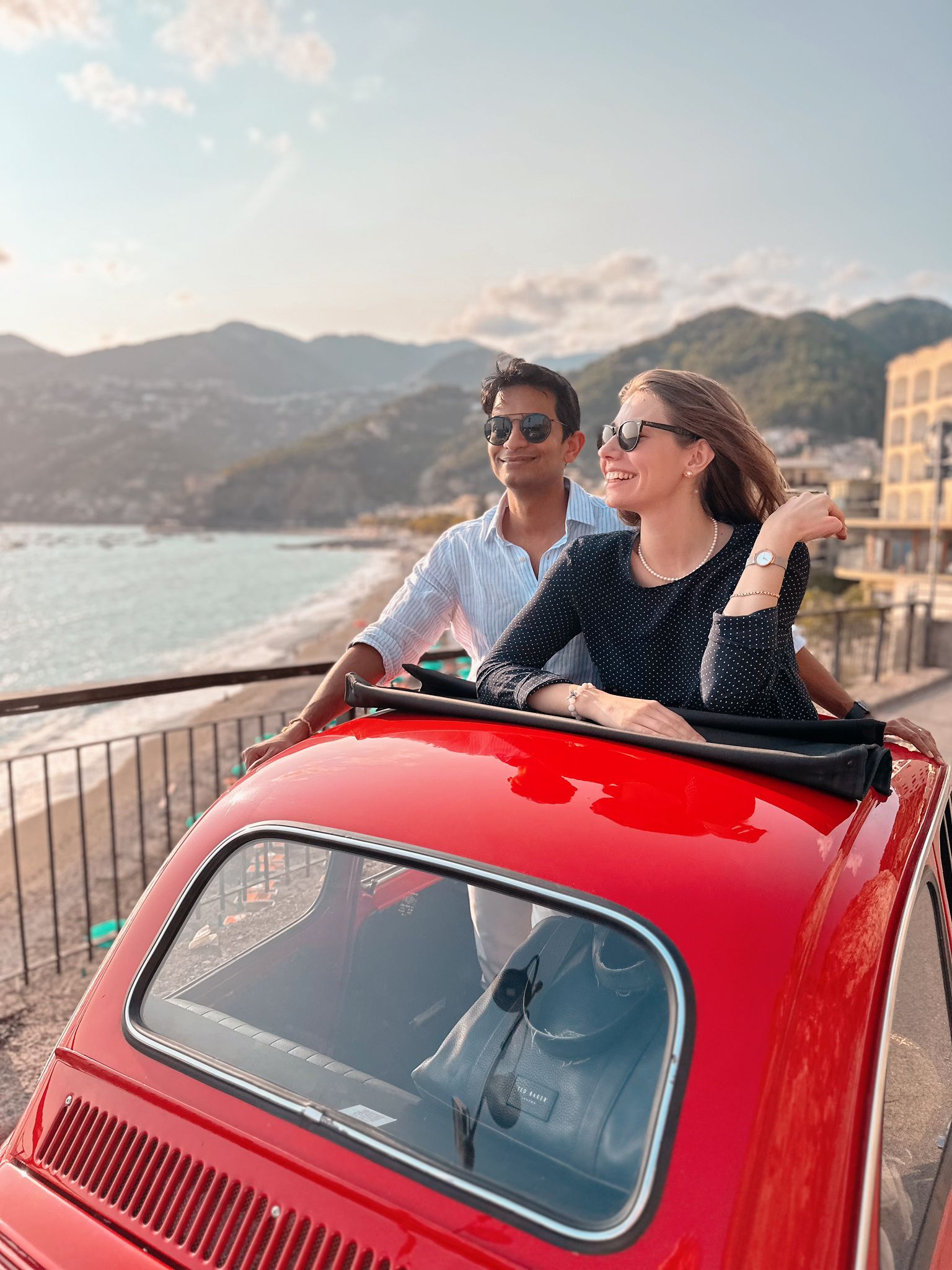 Red vintage car driving along coastal road with ocean view.